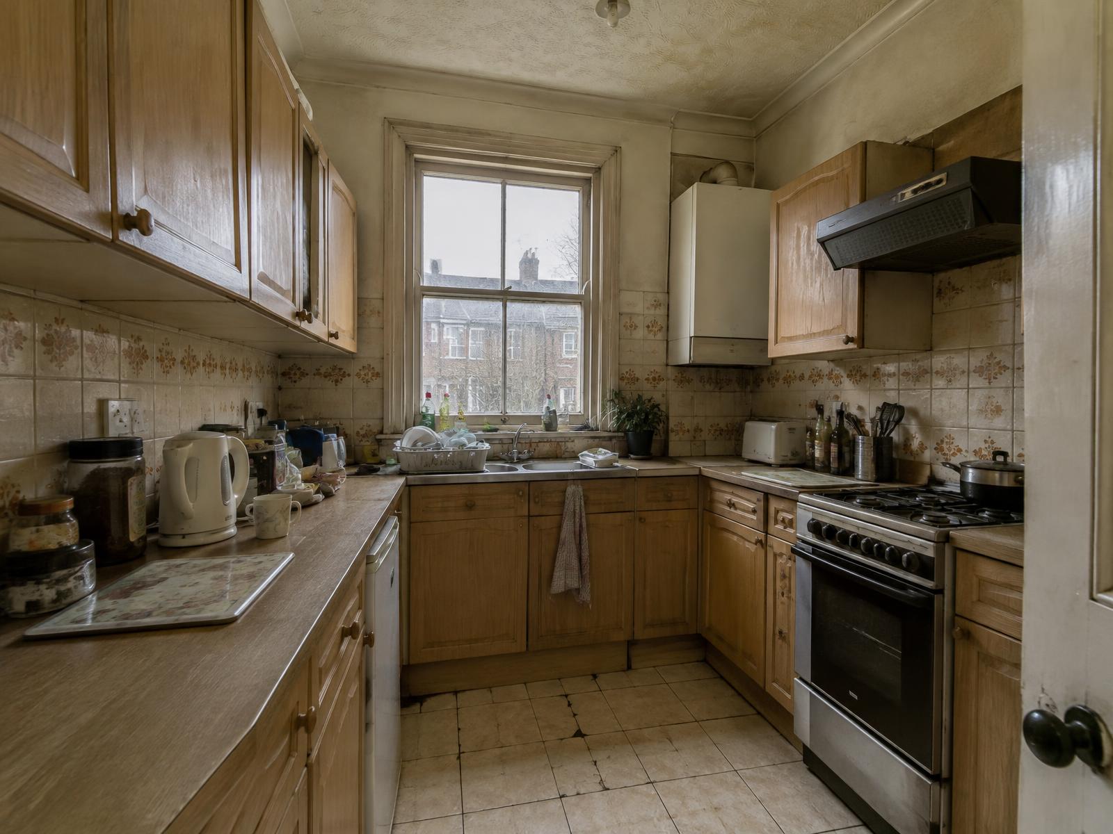 The same Victorian terrace kitchen before renovation, with dated light oak units and cracked floor tiles
