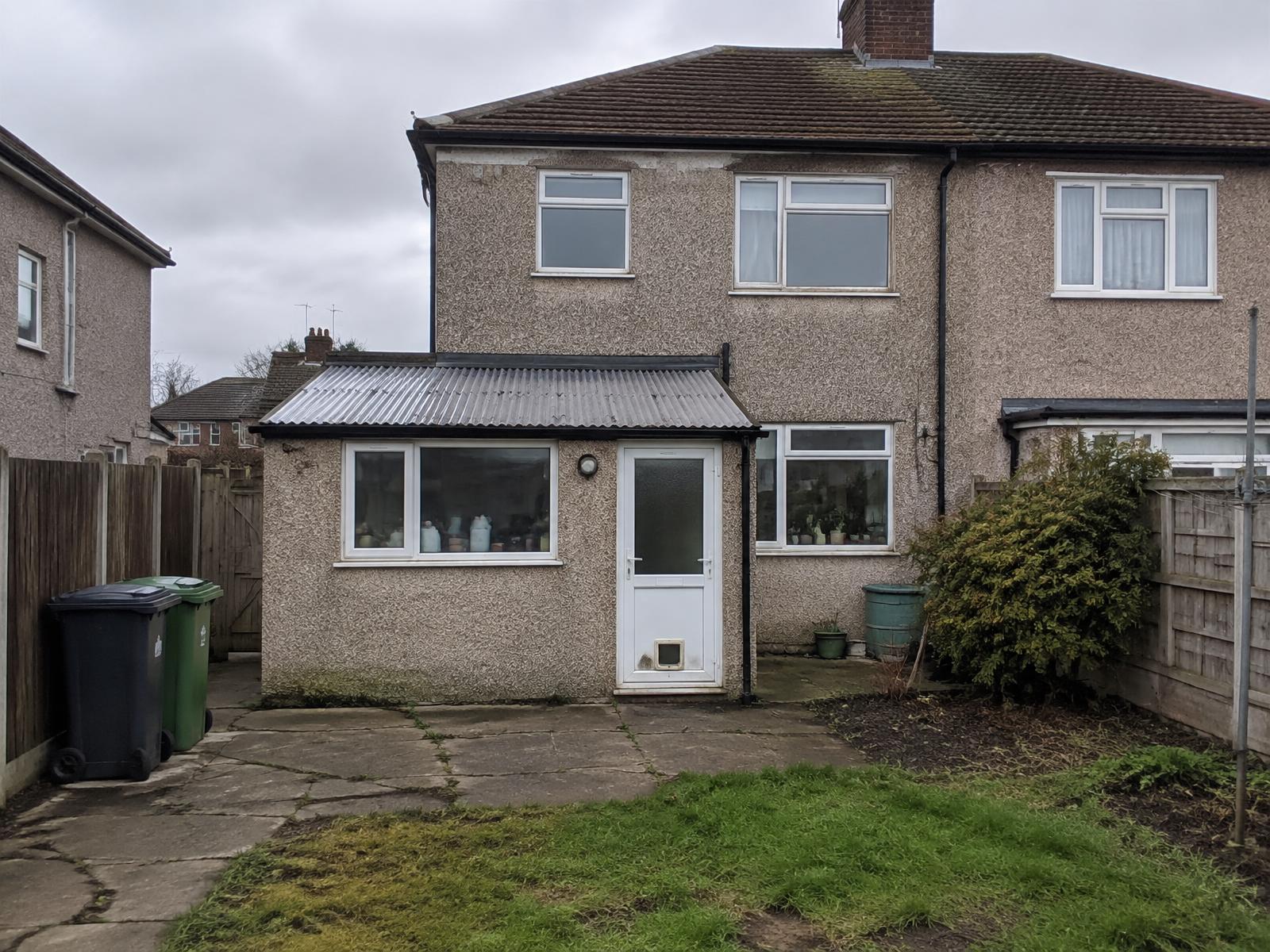 The rear of the same semi-detached house before work, with an old pebble-dashed lean-to and cracked paving